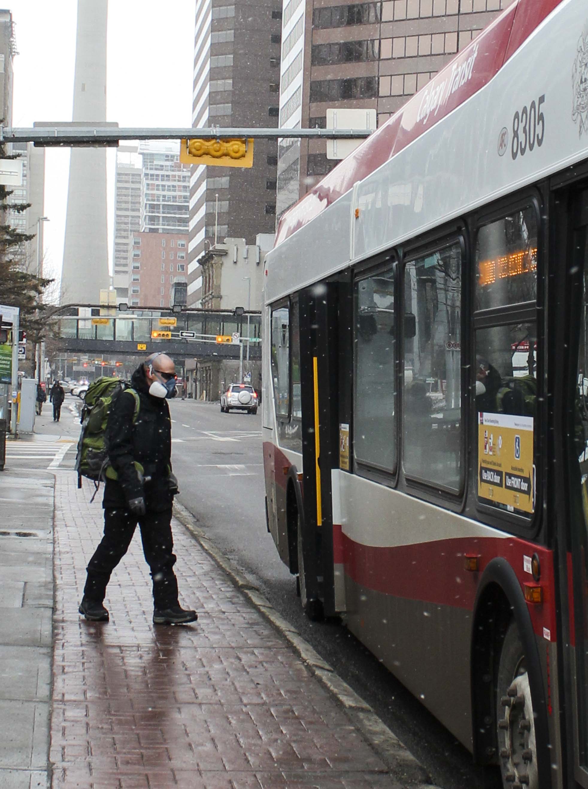 In the midst of COVID-19 pandemic, a man wears a full protective mask and boards a bus from the back door in downtown Calgary on Tuesday, April 7, 2020. People are expected to use an honour system for the transit fare while boarding from the back door to protect the drivers. (Photo by Meng Wei/SAIT)